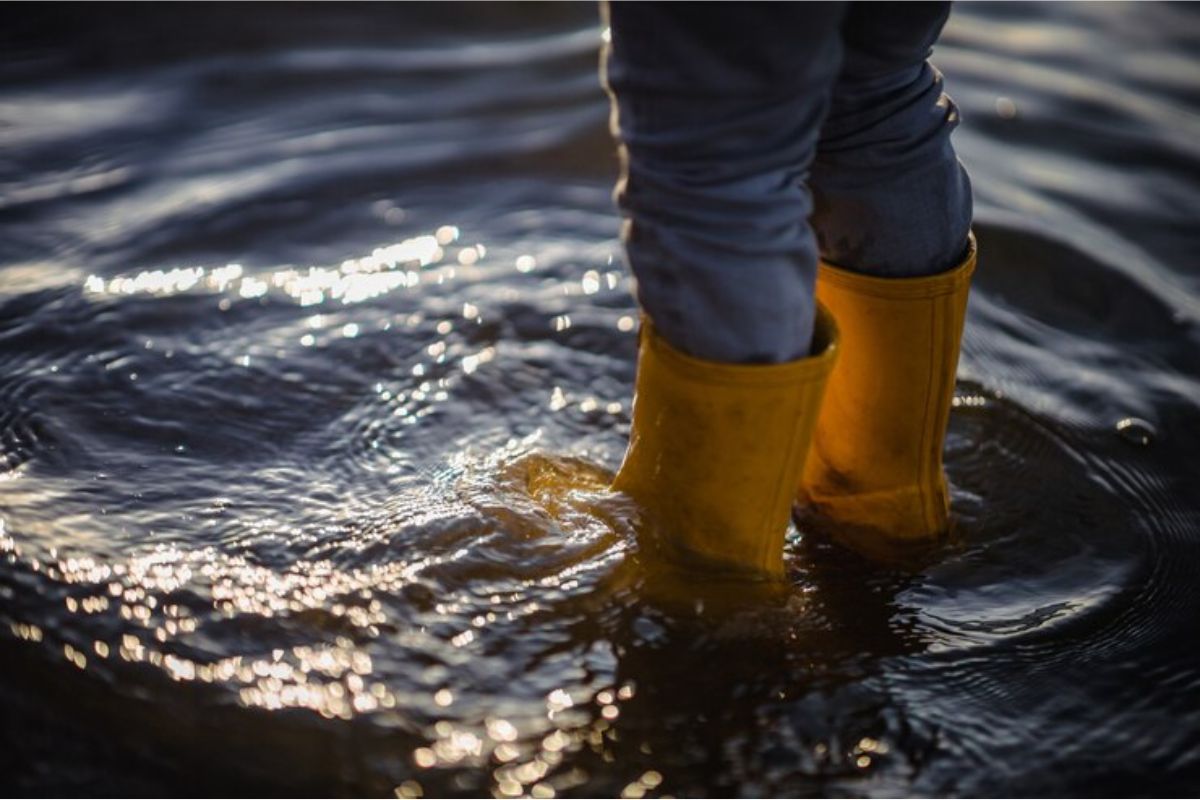 Uma menina com bota amarela pisando em um chão inundado após ver que o Governo Libera R$ 5.100 para Famílias Desabrigadas